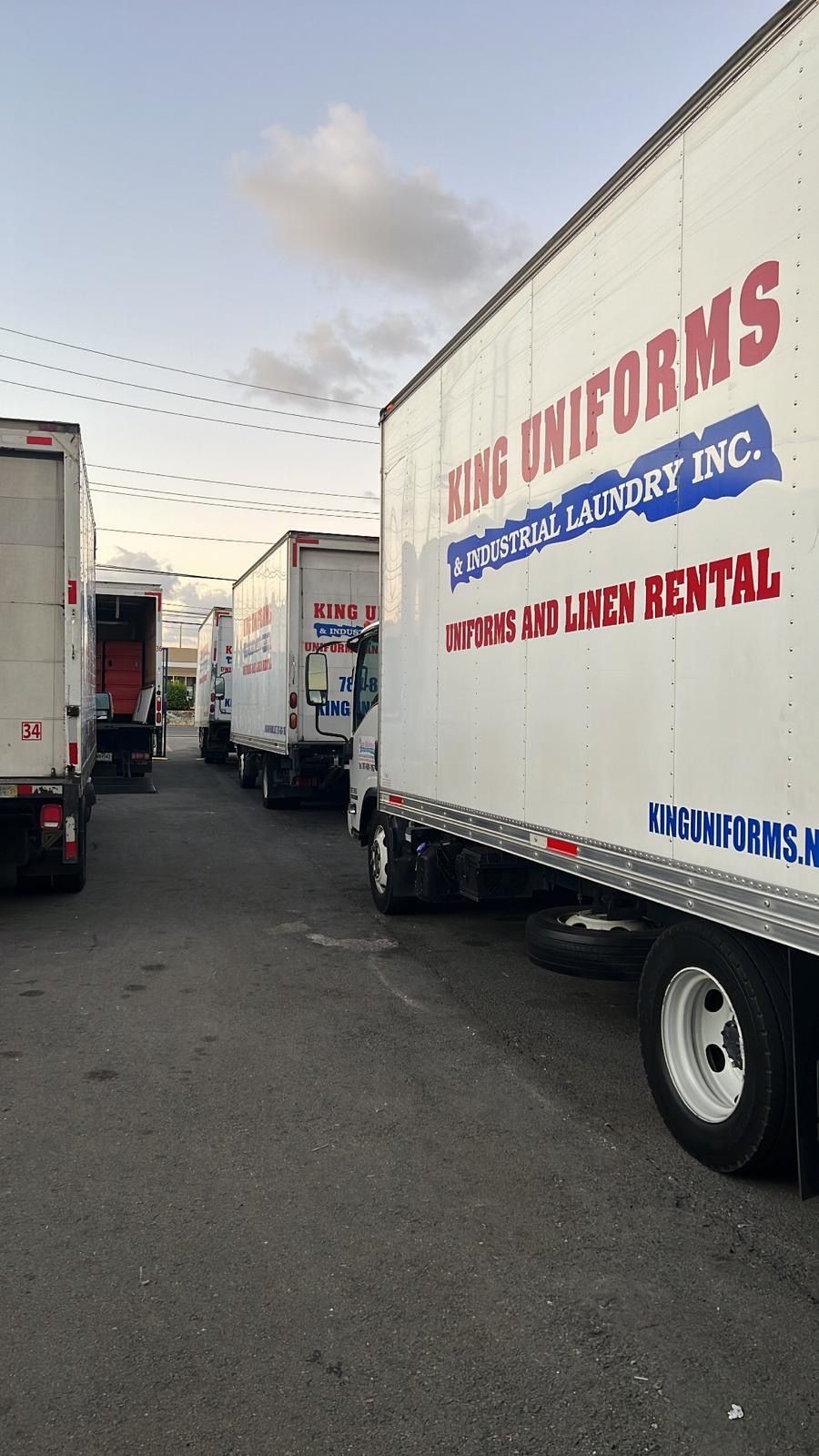 Row of trucks labeled 'King Uniforms & Industrial Laundry Inc.' parked in an industrial area.