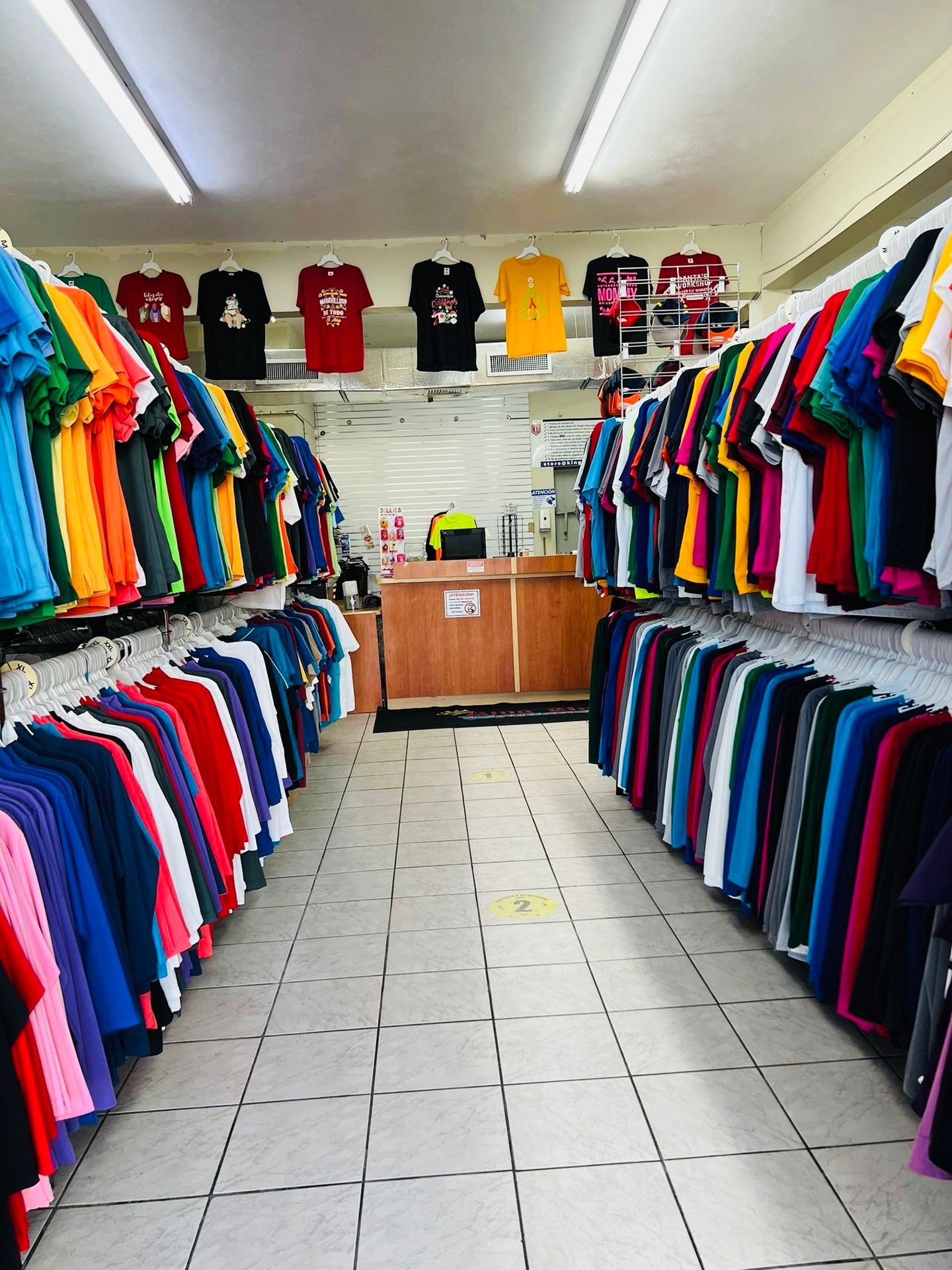 Inside a clothing store with colorful shirts hanging on racks along the walls and ceiling.