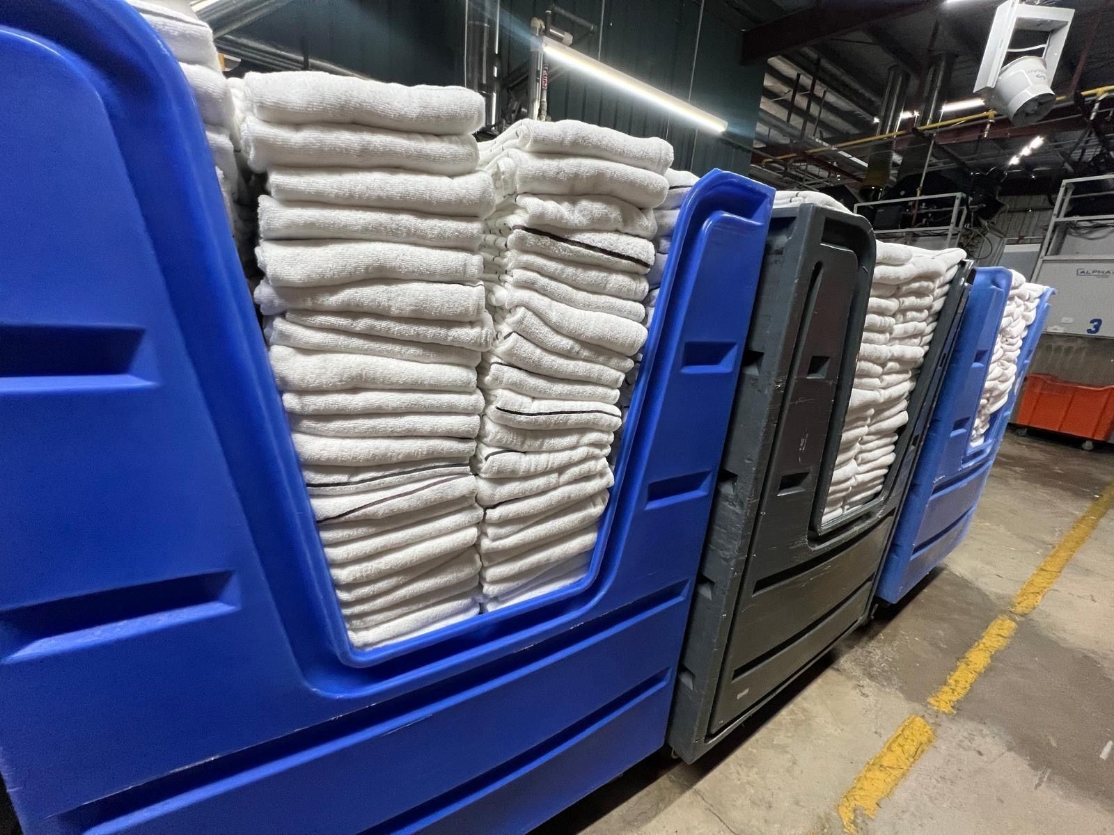 Rows of white folded towels stacked in large blue containers at an industrial laundry facility.